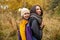Happy young mother with her kid girl on back in ergonomic baby carrier in autumn nature. Babywearing concept
