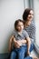 Happy young mother with her upset girl child at home near window