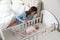 Happy young mother near bedside crib with her newborn baby at home