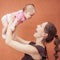 Happy young mother throw up baby on background orange wall