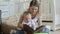 Happy young mother watching family photo album with her baby son on floor at living room