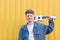 Happy young musician standing with a white ukulele on a yellow background and smiling. Musical concept