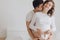 Happy young pregnant couple holding white little socks on belly bump and relaxing on white bed. Stylish pregnant family, mom and