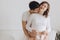 Happy young pregnant couple holding white little socks on belly bump on white bed. Stylish pregnant family, mom and dad in white,