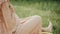 Happy young pregnant woman in a pink dress sitting among green plants and wildflowers. She gently strokes her stomach