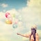 Happy young red hair woman holding colorful balloons and flying on clouds sky background.