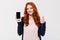 Happy young redhead lady showing display of mobile phone