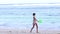 Happy young slim woman in swimwear running on the beach side of ocean with green balloon with smile in slow motion