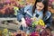 Happy young smiling female working with flowers at greenhouse holding box multicolored plants