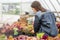 Happy young smiling female working with flowers at greenhouse holding box multicolored plants