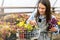 Happy young smiling female working with flowers at greenhouse holding box multicolored plants