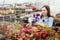 Happy young smiling female working with flowers at greenhouse holding box multicolored plants