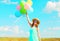 Happy young smiling woman with an air colorful balloons is enjoying a summer day over a meadow blue sky background