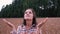 Happy young tourist woman in a plaid shirt looks up with raised arms, enjoying a calm rainy day in nature, breathing