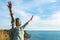 Happy young traveler woman raised arm up to sky enjoying a beaut