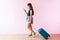 Happy Young Traveler Woman Walking with Suitcase and Music Headphone, Face looking at Smartphone and Smiling, Colorful Pastel