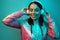 Happy young woman in 90s style sport outfit with white headphones listening to music in neon lights at studio.