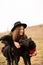 Happy young woman with black hat, plaing with her black dog on the shore of the lake