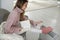 Happy young woman with book warming feet on electric heater at home