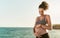 Happy young woman caressing her pregnant belly next the sea