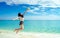 Happy young woman in casual style fashion and straw hat jumping at sand beach. Relaxing and enjoy holiday at tropical paradise