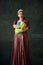 Happy young woman in costume of medieval maid standing with laundry against vintage green background