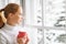 Happy young woman with cup of hot tea in winter window Christmas