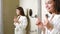 Happy young woman dancing in front of bathroom mirror in the morning. Funny charming woman in white robe dancing happily