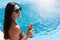 Happy young woman in dark sunglasses holding cocktail while standing next to swimming pool. Female in bikini with leopard print