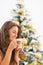 Happy young woman drinking latte macchiato near christmas tree