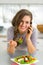 Happy young woman eating greek salad in kitchen