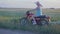 A happy young woman in a hat rides a retro motorcycle and enjoys a ride on a dirt road among the fields and meadows