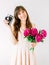 Happy young woman holding in hands bouquet of peonies and old vintage camera. Sweet romantic moment. Smiling woman