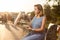 Happy young woman holding hot pizza in box, seat outdoor in park