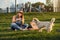 Happy young woman holding hot pizza in box, seat outdoor in park