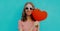 happy young woman holding red heart shaped balloon wearing a sunglasses on a blue background