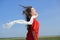 Happy young woman holding white scarf with opened arms expressing freedom, outdoor shot against blue sky