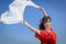 Happy young woman holding white scarf with opened arms expressing freedom, outdoor shot against blue sky