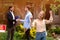 Happy young woman with house key and her husband shaking hands with realtor in backyard