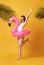 Happy young woman jumping on yellow background dressed in swimwear holding flamingo rubber ring beach