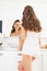 Happy young woman looking in mirror in bathroom