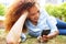 Happy young woman lying in grass at the park and looking at mobile phone