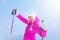 Happy young woman in pink ski jacket holding ski poles in gloves