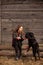 Happy young woman plaing with her black dog in fron of old wooden house. Girl tries a hat to her dog