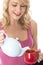 Happy Young Woman Pouring Tea from a Teapot Into Red Mug