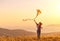 Happy young woman running with kite on glade at sunset in summer