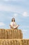 Happy young woman sits in lotus position on huge haystack and meditates. Blue sky background. Countryside holiday