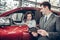 Happy young woman sitting in a new car at car salon professional salesman showing them information on digital tablet couple buying