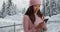 Happy young woman smiling and using smartphone in snow covered park