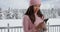Happy young woman smiling and using smartphone in snow covered park